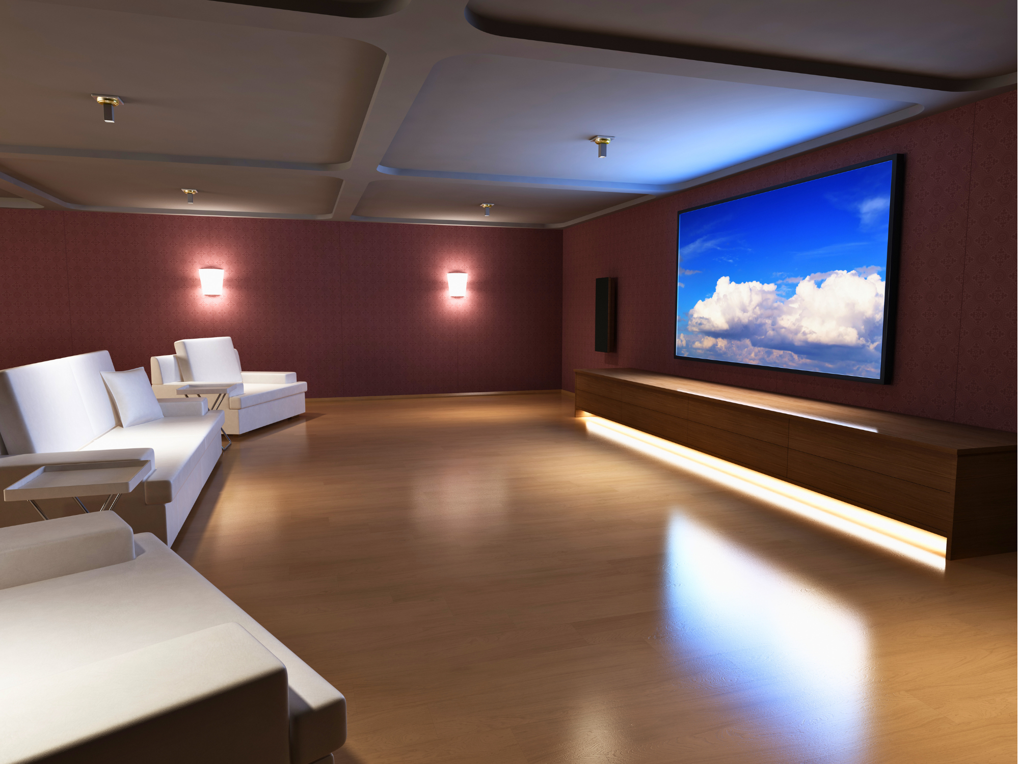 A spacious home theater room with a large flat-screen TV displaying a serene sky with clouds. The room features modern white sectionals and armchairs, ambient wall lighting, wooden flooring, and a sleek low wooden TV cabinet with under-lighting.