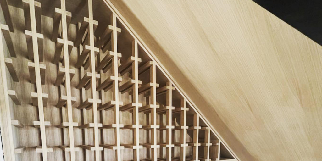 A wooden wine rack with a geometric, triangular design and multiple square compartments, viewed from above. The light wood panels create a pattern of intersecting lines and angles.